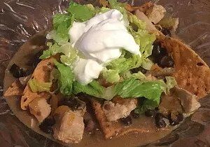 A plate of nachos topped with lettuce and sour cream.