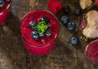 A vibrant red smoothie garnished with fresh berries on a rustic wooden surface.