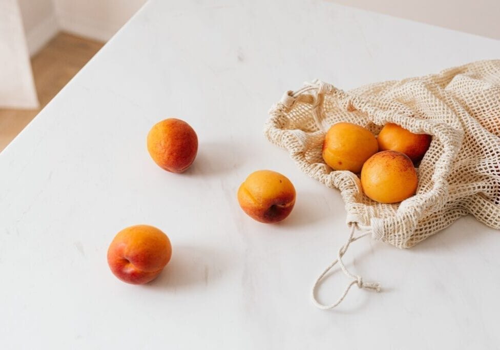 Fresh apricots spilling out of a mesh bag onto a white surface.