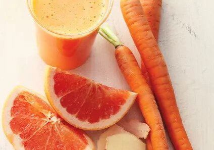 Fresh carrot juice with grapefruit slices and whole carrots.